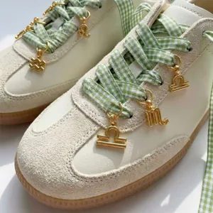 Detail view of golden stainless steel zodiac charms attached to green gingham sneakers laces