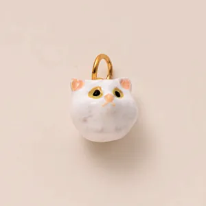 Close-up of a cute handmade white ceramic cat charm with gold loop for DIY accessories