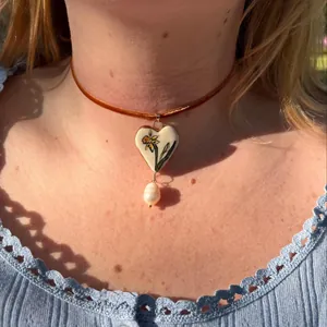 Close-up of cottagecore heart necklace featuring floral painting and a baroque pearl drop