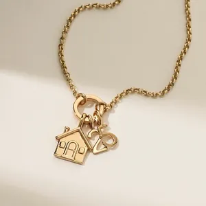 Elegante goldfarbene Halskette mit Haus- und Nummer-25-Anhängern auf strukturiertem Grund.