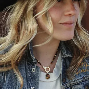 Lifestyle detail shot of a tiger-eye beaded necklace with a teardrop gold pendant.