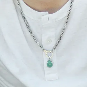 Close-up view of a green teardrop gemstone pendant on a thick silver Byzantine chain