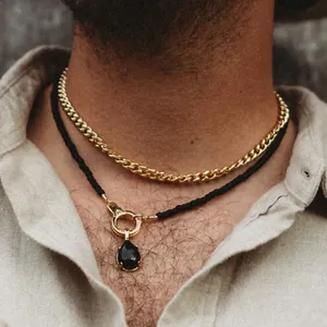 Detailed view of layered gold cuban chain and black teardrop gemstone pendant necklace