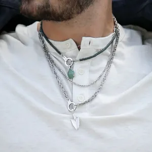 Detail view of a male model wearing layered titanium steel necklaces with green gemstone