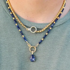 Detail of layered necklaces featuring gold chain and blue beads with a teardrop pendant