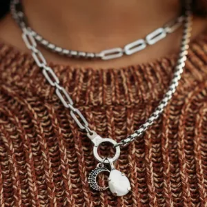 Detail showing white teardrop stone and moon charm on a layered stainless steel chain.
