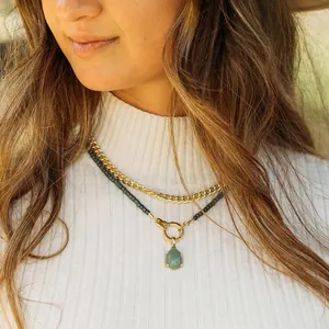 Detailed close-up of a gold cuban link chain and green teardrop gemstone pendant