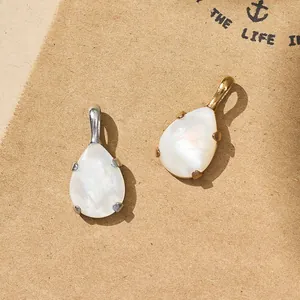 Detail of gold and silver teardrop pendants with white pearlescent inlay on kraft paper.