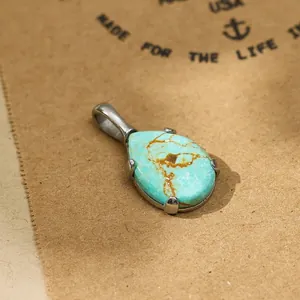 Detail shot of teardrop turquoise pendant in titanium steel on brown paper backdrop