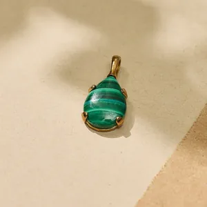 Macro detail of teardrop green malachite pendant set in gold-tone titanium steel.