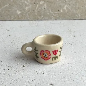Detailed macro view of a miniature cream cup pendant with hand-painted floral patterns.