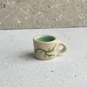 Close-up of a ceramic mug charm with green interior and leafy vine pattern for DIY jewelry