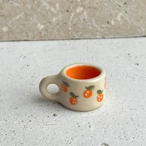Detailed view of a miniature ceramic cup pendant with orange prints for DIY jewelry.