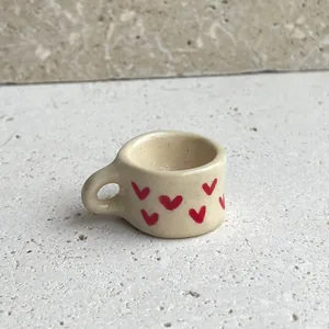 Close-up view of a miniature cream cup pendant featuring vibrant red heart patterns.
