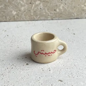 Detailed macro shot of a beige miniature cup charm featuring red Arabic Habibi print