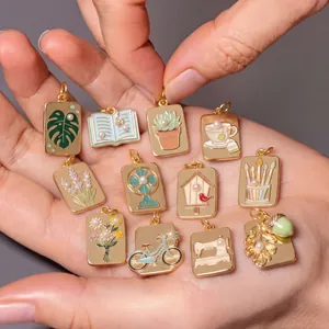 Detailed view of gold enamel pendants with monstera and flower designs held in palm