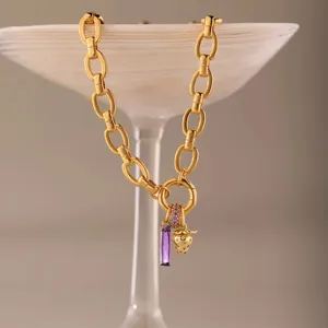 Macro detail of titanium steel gold chain necklace with purple crystal and strawberry charm
