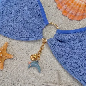 Detailansicht eines Bikini-Accessoires mit goldener Muschel und blauem Delfin-Anhänger.