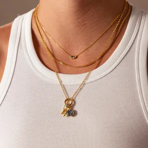 Détail d'un collier doré à plusieurs rangs avec zircon bleu et pendentif lettre M