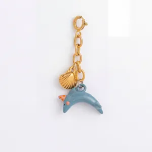 Detailansicht eines goldfarbenen Anhängers mit Muschel und blauem Delphin für Bikinis