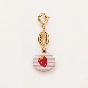 Nahaufnahme eines goldfarbenen Kaurimuschel-Links und Erdbeer-Anhängers für Sommerschmuck