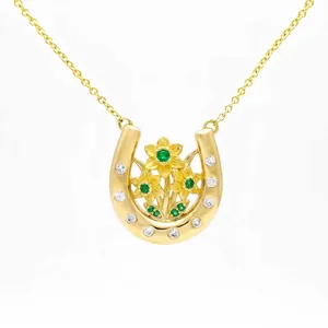 Close-up of golden horseshoe necklace with daffodil flowers and green gemstones