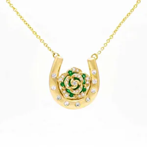 Detailed view of a gold horseshoe necklace with an emerald and diamond rose pendant