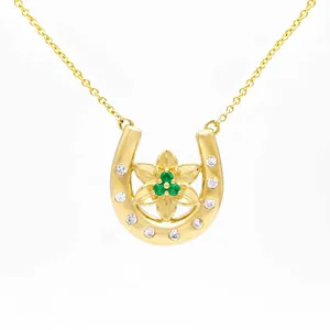Detailed close-up of a gold-plated horseshoe necklace featuring a green gemstone flower center