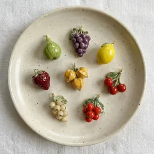 Detailopname van acht verschillende fruitvormige bedeltjes op een gespikkeld beige bord