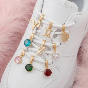 Gros plan de pendentifs zodiaque et pierre de naissance dorés 18 carats sur baskets blanches.