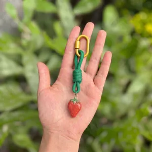 Detailed view of a handmade strawberry pendant with a green knotted rope bag charm