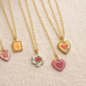 Gros plan de pendentifs vintage en céramique peints à la main sur chaînes dorées.