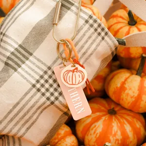 Macro view of a hand-painted pumpkin keychain charm attached to a checkered canvas bag