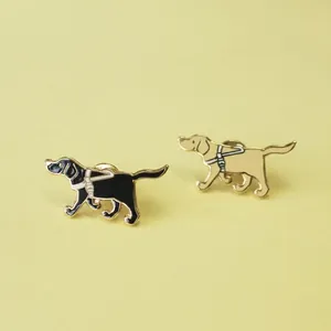 Detailed view of black and tan Labrador guide dog enamel pins on a yellow surface