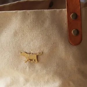 Close-up detail of golden Labrador guide dog metal enamel brooch pinned on a beige canvas bag