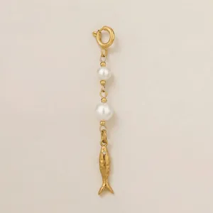 Detail showing a golden fish charm and white pearls on a stainless steel link chain