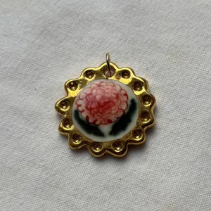 Detailed macro view of a vintage golden floral ceramic pendant on white linen background.