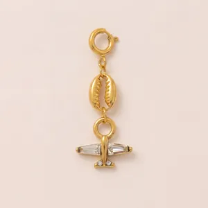 Detailed view of a gold airplane charm with sparkling crystals and a cowrie shell pendant