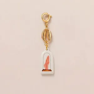 Detail of golden cowrie shell charm with white ceramic hand illustration pendant.