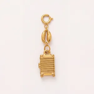 Detailed view of a golden vintage suitcase and cowrie shell jewelry charm pendant