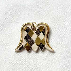 Macro view of a ceramic wing pendant with gold edges and a hand-painted harlequin pattern