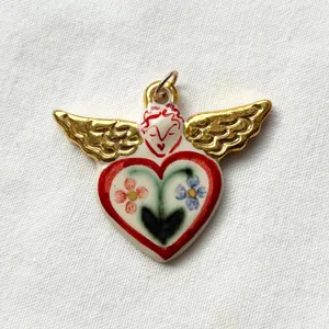 Detailed macro shot of a handmade angel heart pendant with gold wings on white linen.
