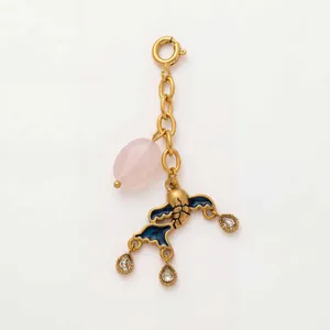 Detailansicht eines vergoldeten Anhängers mit rosa Stein und blauer Emaille-Vogelform.