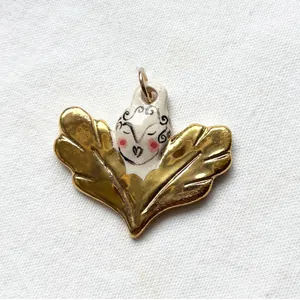 Detailed close-up of a unique golden winged pendant with a hand-painted ceramic face