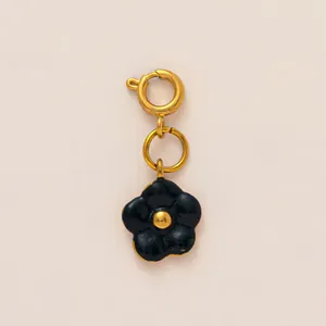 Detailed view of a black enamel flower charm with a golden spring ring clasp attachment