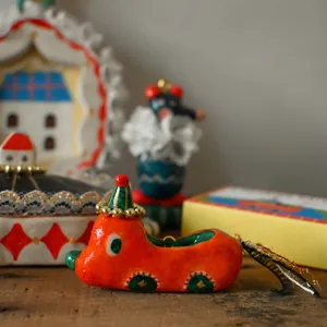 Close-up of a whimsical orange car figurine with green accents and gold bead details.