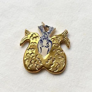 Close-up detail of a gold stainless steel pendant featuring mermaid and wing motifs.