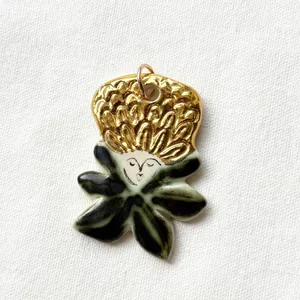 Unique artistic ceramic and gold-toned pendant featuring a minimalist face and leaf design.