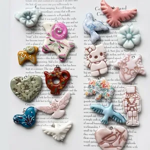 Assorted ceramic bird heart and flower charms for DIY jewelry making on book background