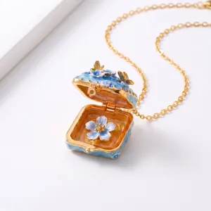 Detailopname van open emaille medaillon ketting met blauwe bloemen en vlinderdetails